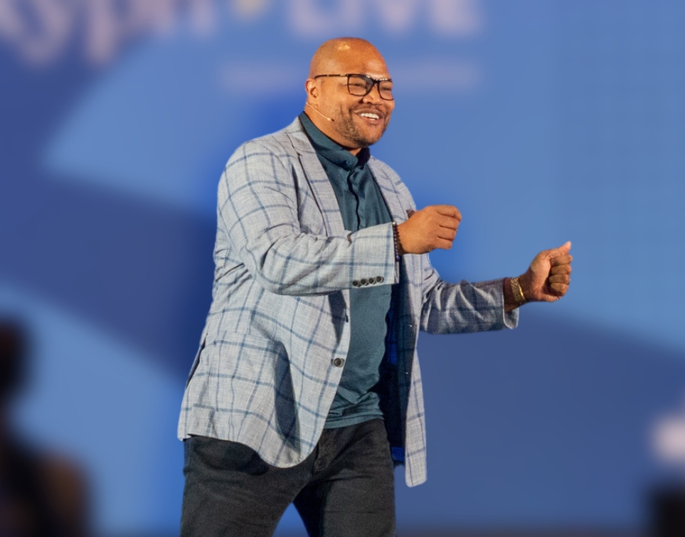 Dr. Preston Cherry in a plaid blazer presenting on stage with a headset mic, delivering a talk on wealth management or personal finance.