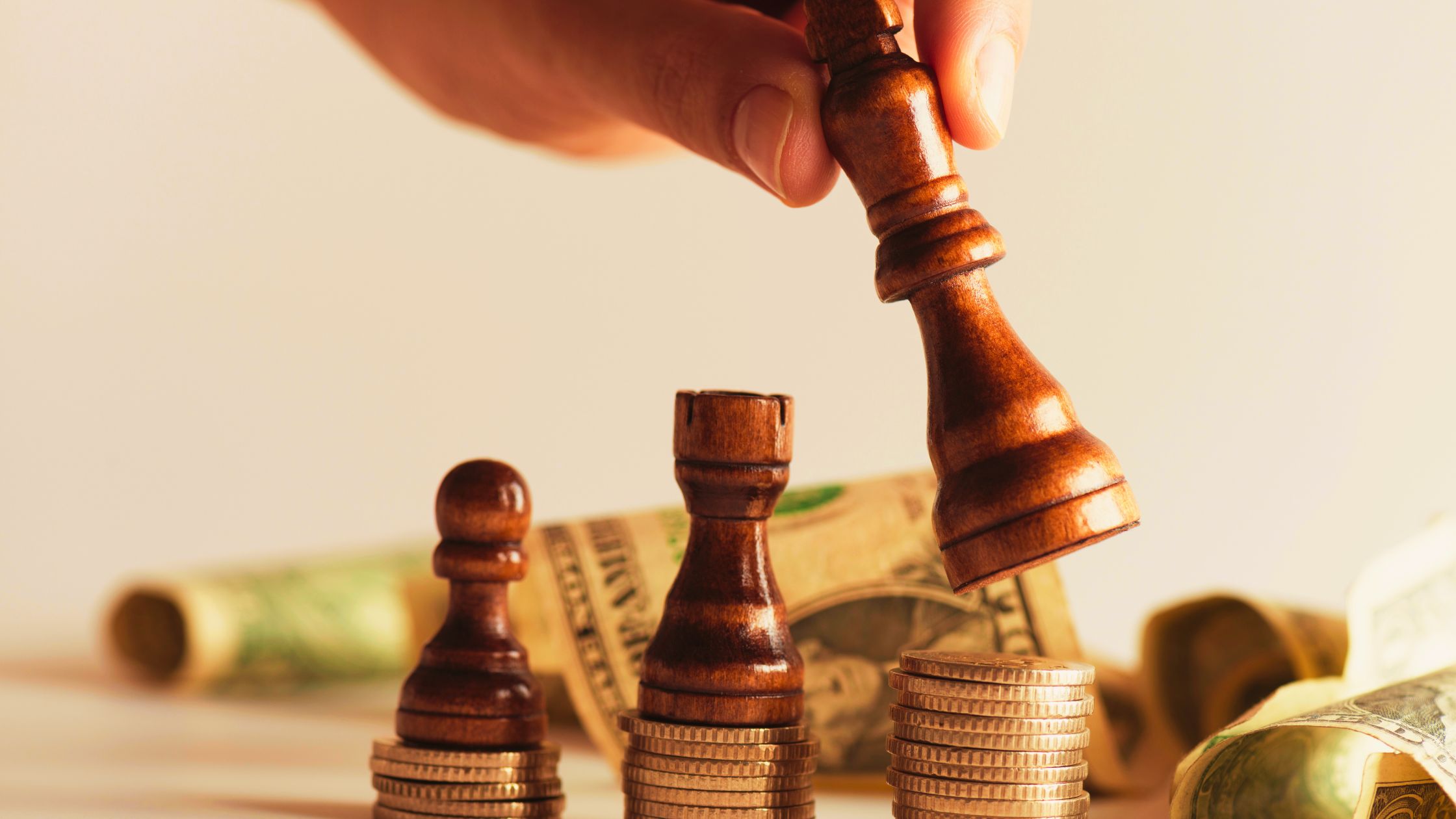 Chess pieces on stacked coins and U.S. dollar bills symbolizing financial strategy during economic uncertainty.